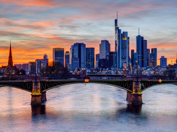 Frankfurter Skyline mit Hochhäusern und einer Brücke über den Main bei Sonnenuntergang